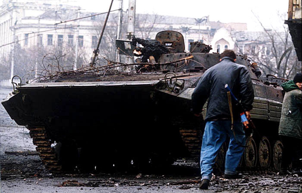 לוחם צ'צ'ני רץ בסמוך לנגמ"ש רוסי שרוף במהלך הקרב על גרוזני   מקור: ויקיפדיה (מיכאיל אבסטאפייב)